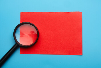 Flatlay picture of magnifying glass and copyspace red paper.