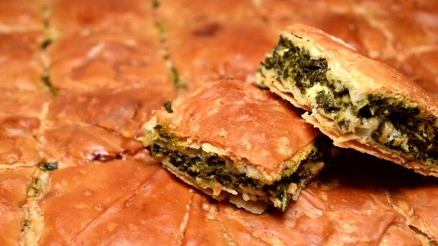 two pieces of spanakopita (spinach pie) on whole pie rotating