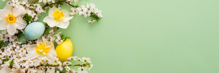 Festive banner with spring flowers and Easter eggs, white daffodils and cherry blossom branches on a green pastel background - Powered by Adobe