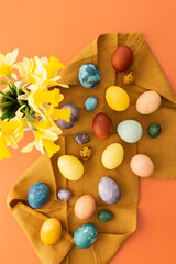 Top view of napkin with dyed natural dyes Easter eggs, bouquet with yellow daffodils in vase on orange background