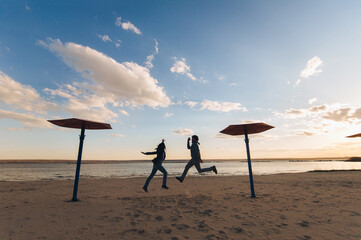 A young couple, a girl and a guy in jeans jumped at the same time, spreading their legs and arms, on the bank of a river (lake). The concept of friendship between lovers and outdoor exercise.