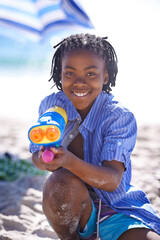 Child, water gun and beach to play, portrait and happy with sand, fighting and swimwear for summer...