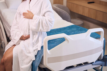 Partial pregnant woman embracing her belly on medical couch in clinic room