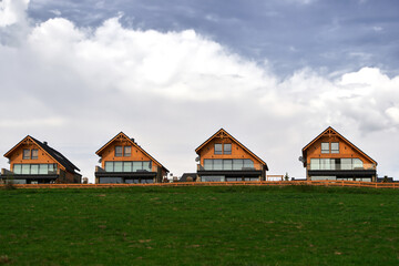A row of modern wooden houses nestled on a lush green hill under a cloudy sky offering a blend of nature and architecture.