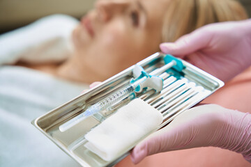 Fototapeta premium Close up of syringe in tray in hands of beautician near blurred woman client