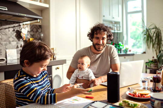 Father spending time with son doing homework and baby in kitchen at home