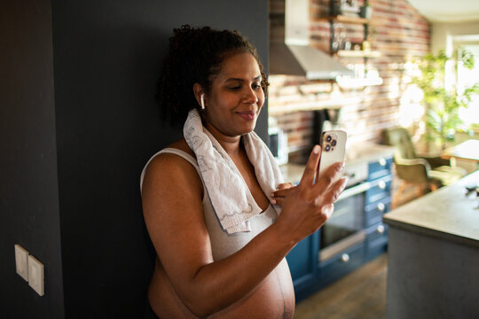 Happy pregnant woman using smartphone after home workout