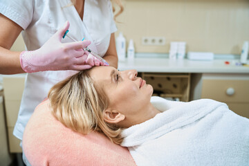 Obraz na płótnie Canvas Partial cosmetologist doing face beauty injection of woman wearing bathrobe