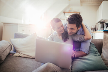 Happy young couple using laptop on sofa at home