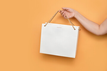 A woman's hand on an orange background holds a paper bag by the handle, a woman is going shopping for clothes, shopping concept
