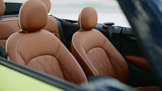 Front passenger and driver seats in premium brown leather interior of Mini Cooper Convertible guaranteeing comfort and safety while driving compact car with roof down