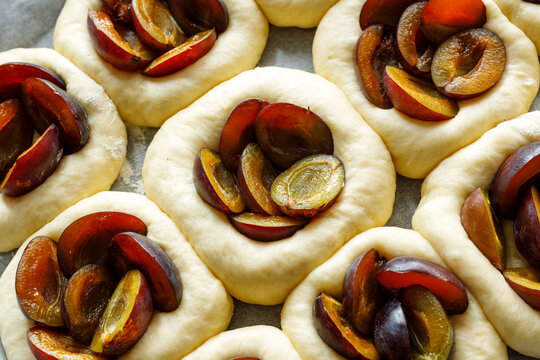 Raw plum yeast buns prepared for baking, focus on the bun inside. Traditional pastries