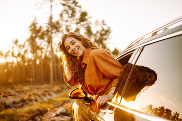 Young happy woman leaning out of the car window enjoying travel. The concept of active lifestyle,...