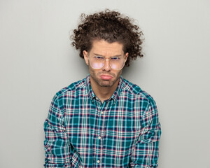 upset cute young man with glasses and curly hair being sad and looking forward