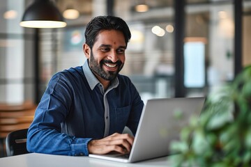 Happy Indian business man looking at laptop using computer working in office. Smiling busy professional businessman employee or company executive cheerful about online project goals, Generative AI - obrazy, fototapety, plakaty