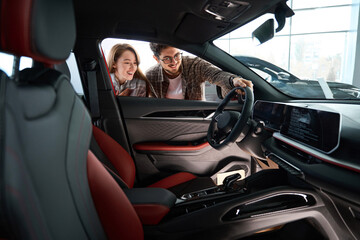 Woman with man look inside of car at dealership choosing suitable vehicle model