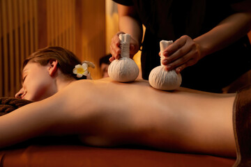Hot herbal ball spa massage body treatment, masseur gently compresses herb bag on couple customer...