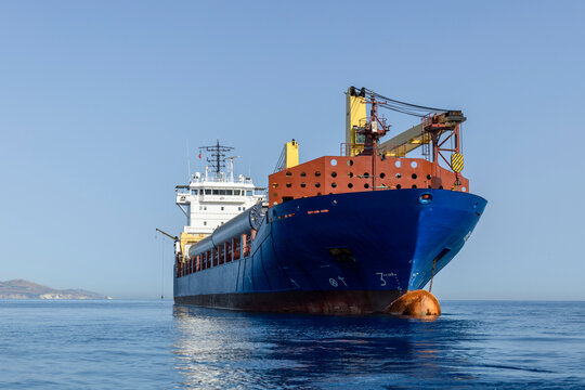 Blue dry cargo ship at sea. Multi purposes vessel carrying wind generators at anchor. View from sea level.