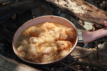 Frying fish and chicken tempura in a pink Teflon pan using wood as fuel creates a unique and flavorful cooking experience.