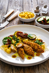 Fried chicken breast fillet with gnocchi and sun dried tomatoes on wooden table