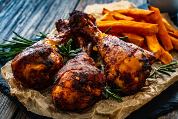 Roasted chicken drumsticks with French fries on wooden table