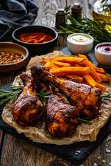 Roasted chicken drumsticks with French fries on wooden table