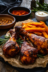 Roasted chicken drumsticks with French fries on wooden table