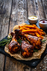 Roasted chicken drumsticks with French fries on wooden table