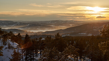 Breathtaking sunset over Lake Krøderen, Norway, framed by snow-covered trees, mountains, and forests. A captivating scene showcasing the stunning natural beauty of this popular tourist destination