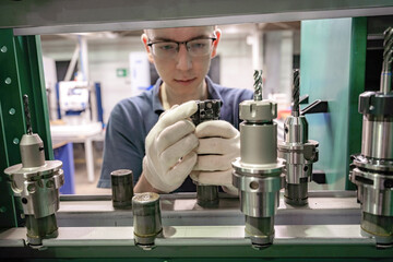 A working machine operator inspects a cutter for a CNC machine from a tool rack.