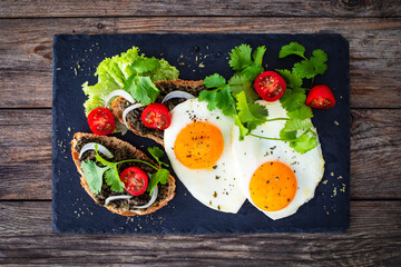 Breakfast - sunny side up egg, tapenade bruschetta and fresh vegetables on wooden table