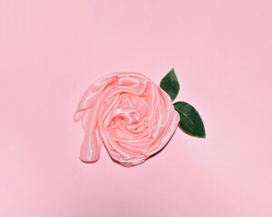 Silk wet scarf folded into the shape of a rose decorated with green leaves, creative, minimal floral composition