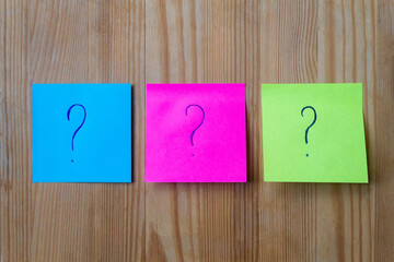 Multicolored post-it sticky notes on the wooden background with question signs