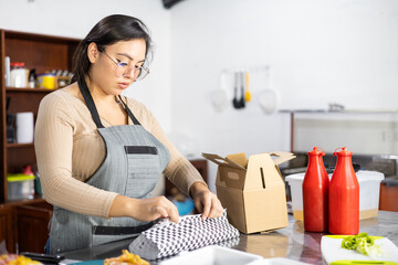 woman packing a hamburger in a cardboard box, fast food ready for delivery, customer service and restaurant lifestyle, dark kitchen service
