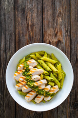 Penne with basil pesto sauce and grilled chicken breast on wooden table
