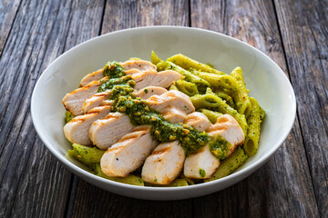 Penne with basil pesto sauce and grilled chicken breast on wooden table