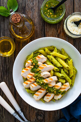 Penne with basil pesto sauce and grilled chicken breast on wooden table
