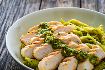 Penne with basil pesto sauce and grilled chicken breast on wooden table
