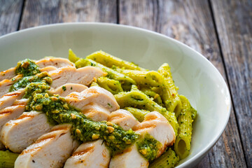 Penne with basil pesto sauce and grilled chicken breast on wooden table