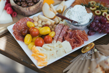 Plate of sliced salami, cheese, apples and tomatoes.