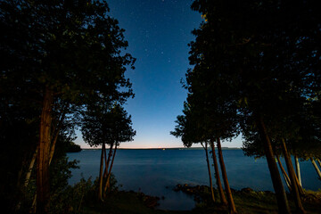 View of night Lake Manitou from the cabin. Dark sky line with stars, landscape with trees and...