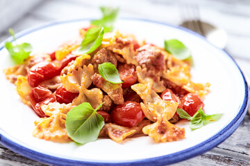 Farfalle pasta with chicken breast, cherry tomatoes and fresh basil. Bright wooden background. Close up.	
