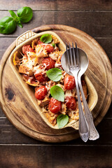 Baked farfalle pasta with chicken breast, cherry tomatoes and mozzarella cheese. Rustic wooden background. Top view.	