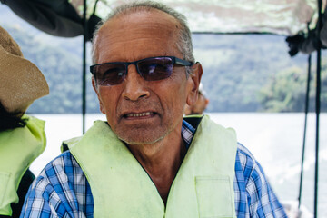 pensioner senior man with glasses wearing life jacket sailing on a river in a boat on vacation