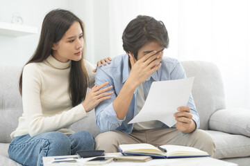 Stressed financial owe asian young couple love hand in holding bills, sitting on sofa together, stressed and confused by calculate expense, mortgage or loan. Debt, bankrupt or bankruptcy people.