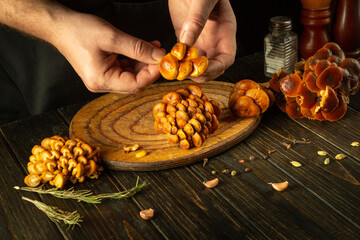 Male hands sort or clean fresh Flammulina velutipes on a wooden kitchen board. The concept of...