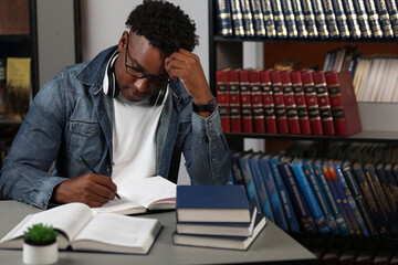 Young man, a student, writes an essay, sits at a table in a modern library at the university. An...