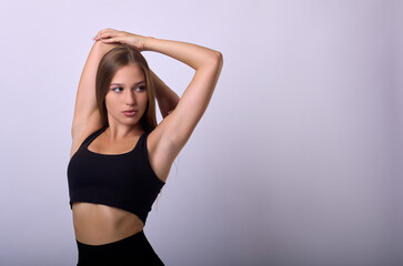 Fototapeta premium Advertising of sportswear in a sports store. Slender young pretty model with long hair in black short tank top raised her hands up, posing for camera. 