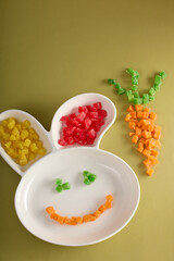 On children plate in shape hare's head made delicious colored candied fruits, smile and shape carrot laid out. Beautiful funny serving children's plate with delicious sweet sweets from candied fruits