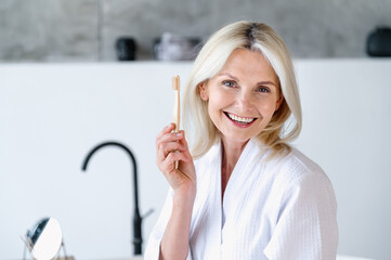 Mature woman hold wooden toothbrush in hand and smile